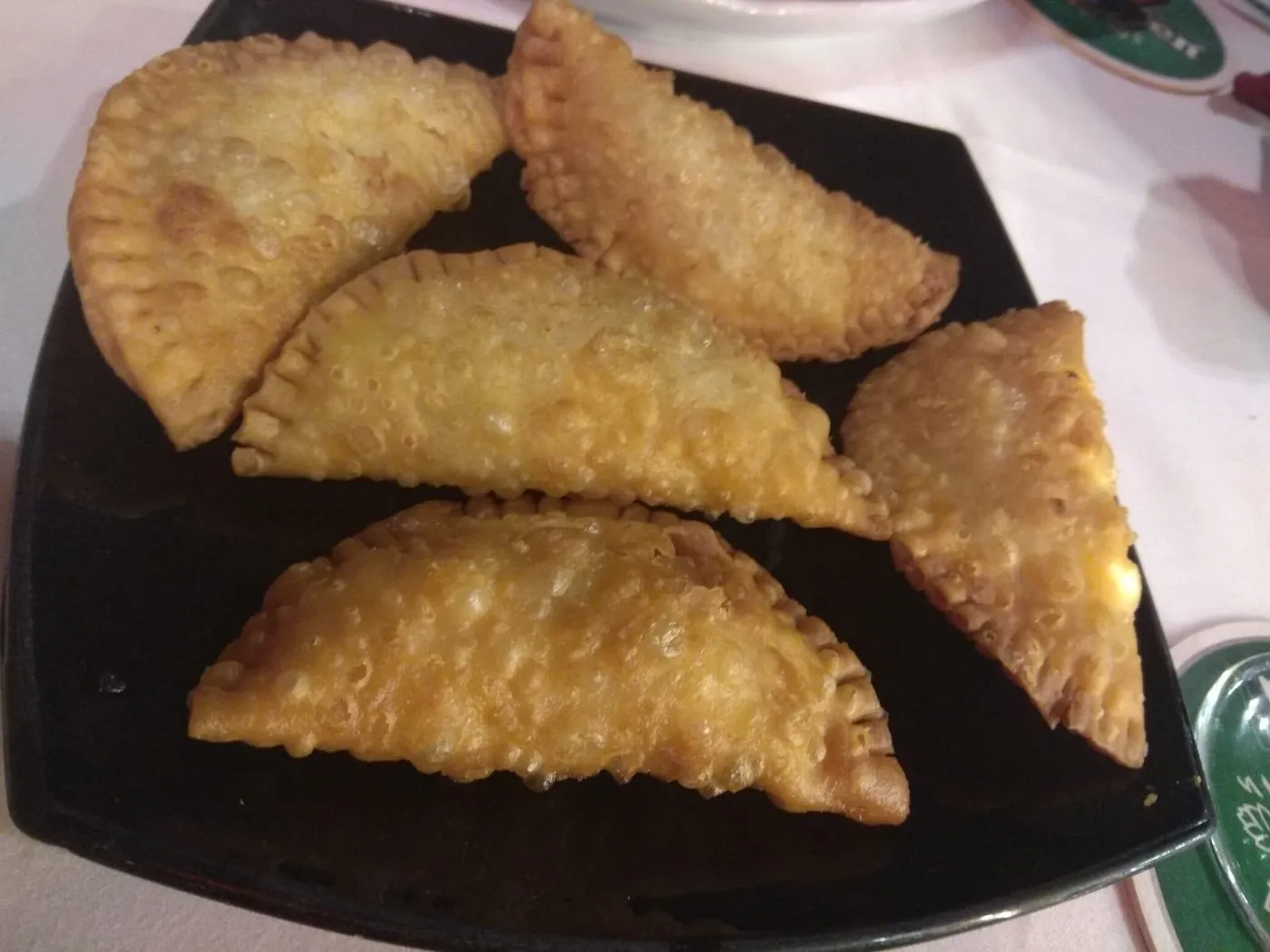 Empanadas fritas doradas en un plato negro, con una textura crujiente y rellenas de ingredientes sabrosos. Ideal para aperitivos o platos principales en la gastronomía latina.