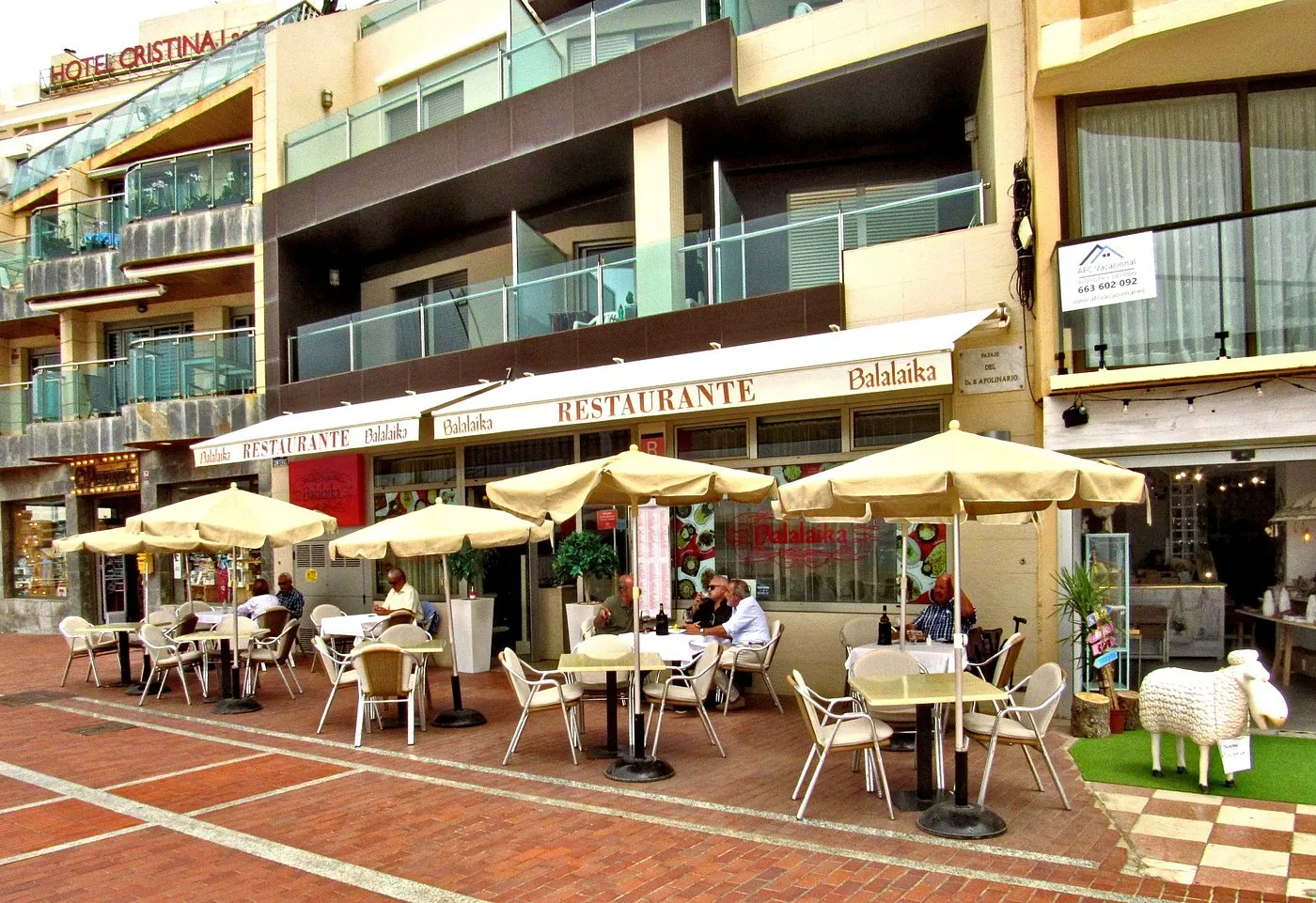 Restaurante Balalaika con mesas al aire libre y sombrillas en una calle peatonal, rodeado de edificios y tiendas. Ideal para disfrutar de una comida en un ambiente relajado.